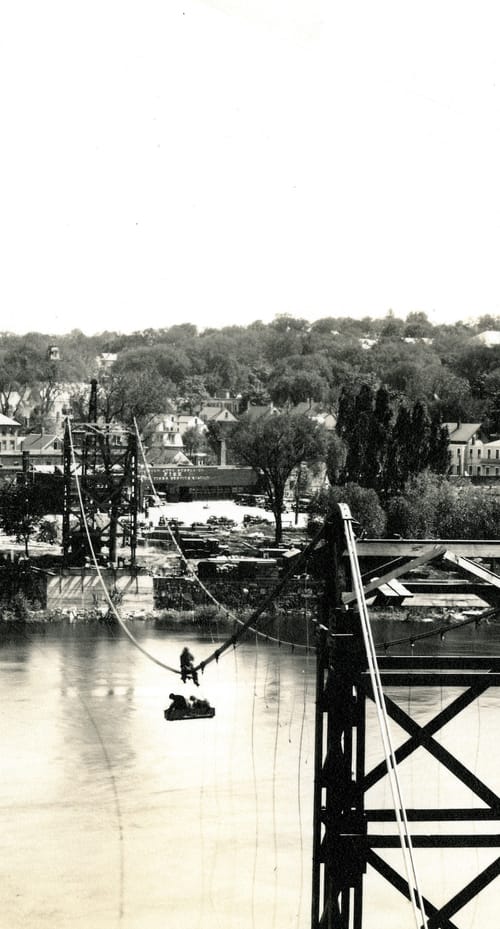 B&W photo of workers suspended over the Merrimack River during bridge construction, courtesy the US National Park Service.